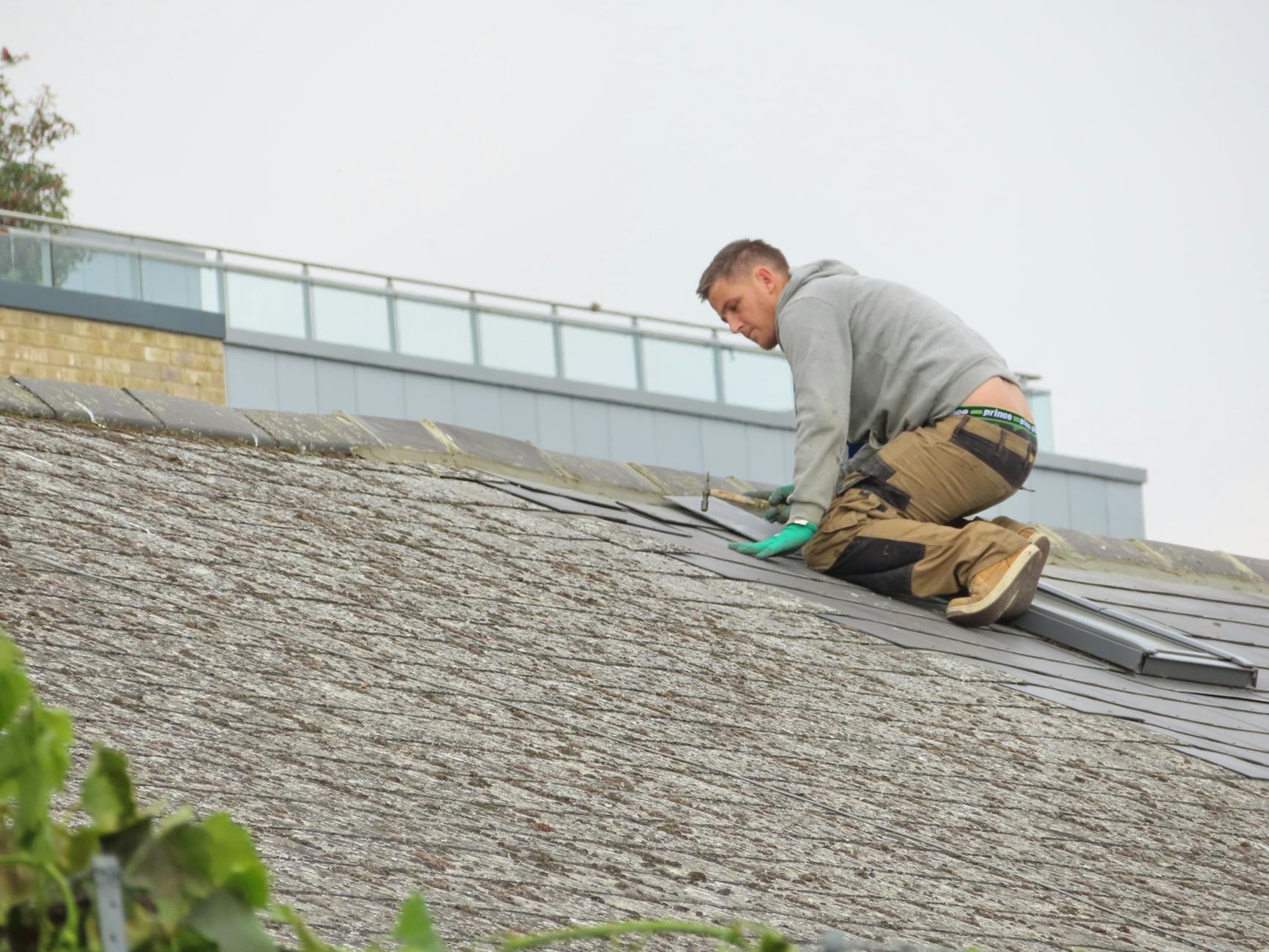 Roofer kneeling on a roof carrying out a repair