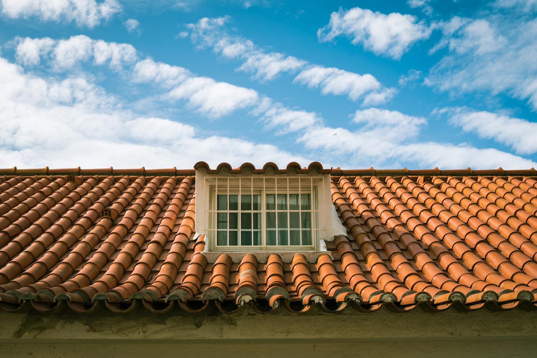 Spanish clay tile roof with a dormer window under a blue sky